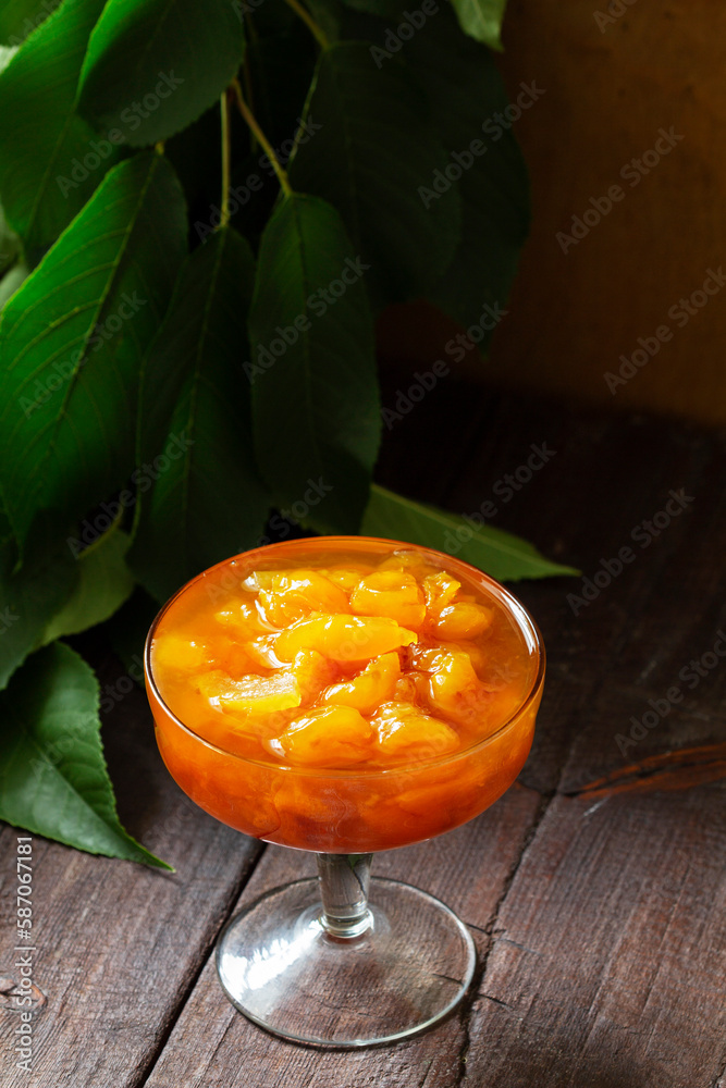 Yellow cherry jam with lemon and vanilla in a glass bowl on a wooden background.