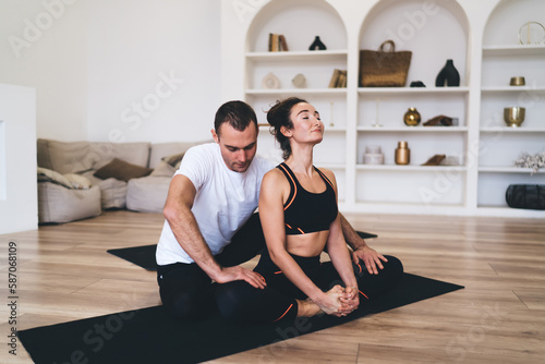 Man helping woman stretching legs for lotus pose
