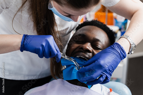 Dentist placing cofferdam in jaw of african man for treatment teeth in stomatology. Dentist using dental dam for tooth isolation. photo