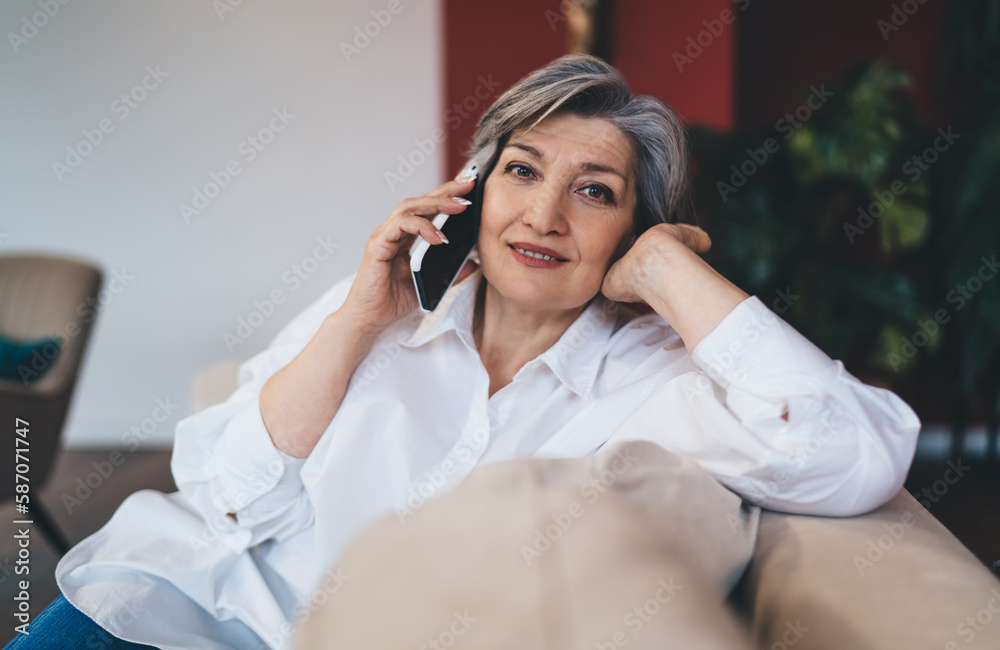 Smiling mature woman talking on smartphone on sofa Smiling mature woman talking on smartphone on sofa