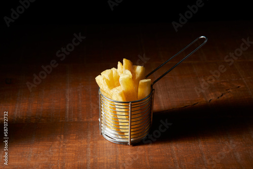 Porção de mandioca frita em pote aramado em fundo de madeira. photo