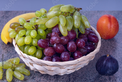 berries of white and red grapes and fresh fruits in a straw basket on a dark wooden background
