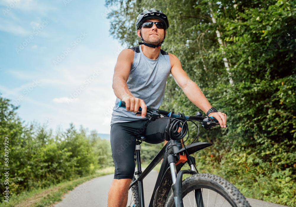 Portrait of happy man dressed in cycling clothes, helmet and sunglasses riding a bicycle on the out-of-town bicycle path. Active sporty people concept image.