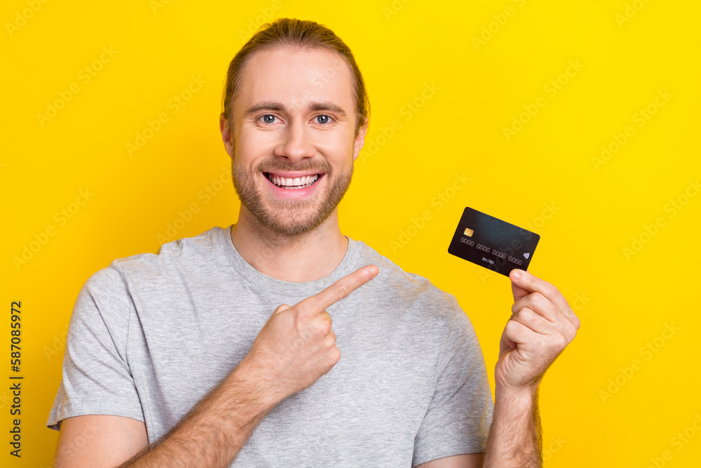 Photo of cheerful positive man wear grey t-shirt pointing finger credit card isolated yellow color background Photo of cheerful positive man wear grey t-shirt pointing finger credit card isolated yellow color background