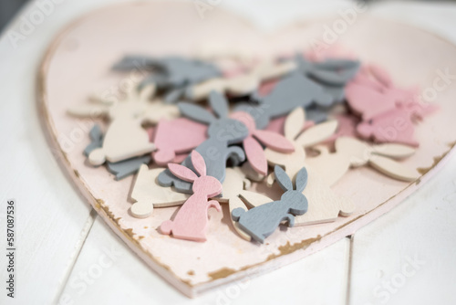 Beautiful playful white, pink and gray wooden Easter bunny figurines on an antique white wooden heart shaped tray on a white wooden table.