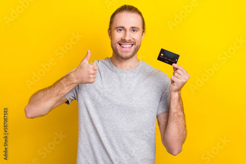 Photo of cheerful satisfied man wear trendy grey clothes thumb up recommend use nfc function isolated on yellow color background
