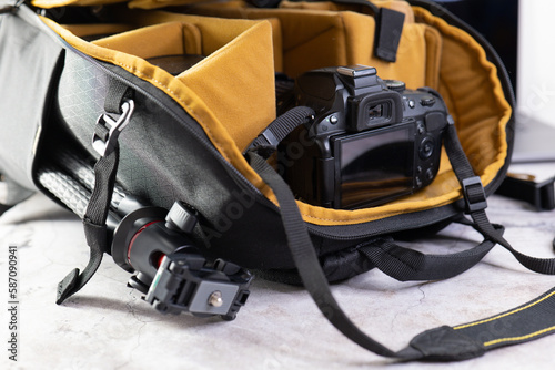 Stylish Camera Bag with Accessories on Grey Table. Professional Camera Equipment. Сamera bag with a mustard yellow interior is displayed open on a grey table, with camera accessories such as lenses