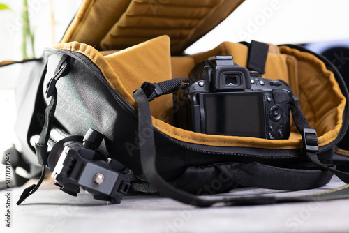 Stylish Camera Bag with Accessories on Grey Table. Professional Camera Equipment. Сamera bag with a mustard yellow interior is displayed open on a grey table, with camera accessories such as lenses © ArtyomPoly's
