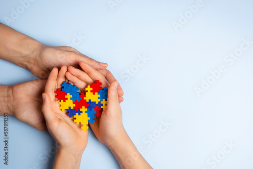 Bild auf Leinwand Woman and child hands holding together colorful puzzle heart on light blue background