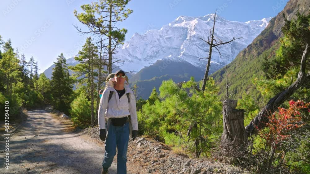 Front view of smiling trekker walking on Annapurna Circuit trail path with picturesque alpine mountains and snowy peaks, Nepal Front view of smiling trekker walking on Annapurna Circuit trail path with picturesque alpine mountains and snowy peaks, Nepal