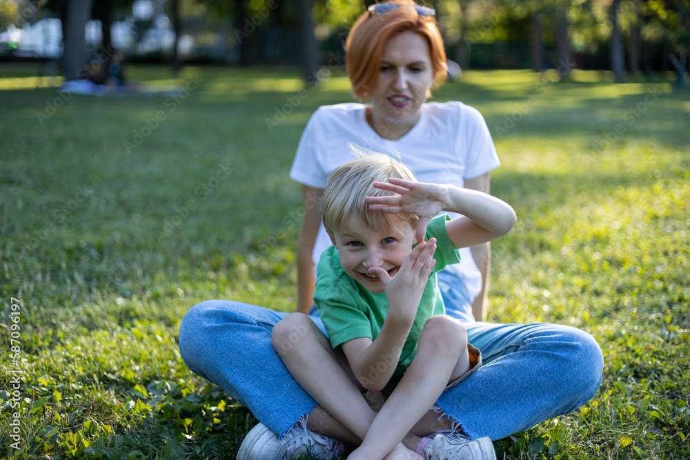 Fototapeta premium Red haired happy mother having fun with her blond haired laughing son in park