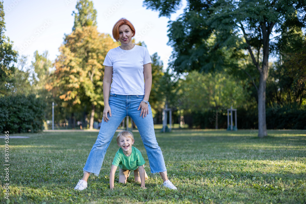 Red haired happy mother having fun with her blond haired laughing son in park