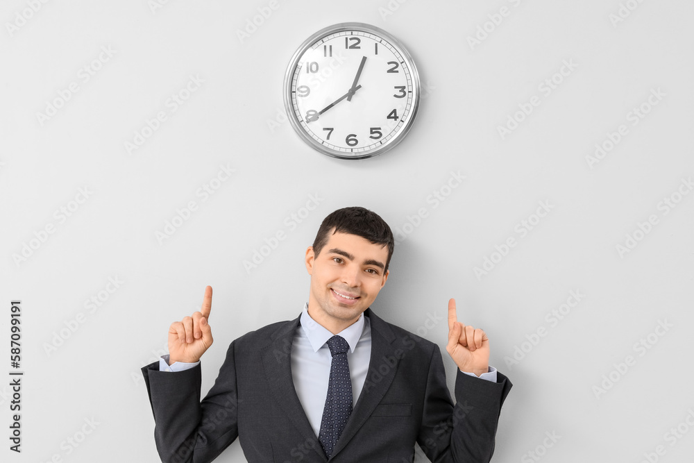 Young businessman pointing at clock on light wall Young businessman pointing at clock on light wall