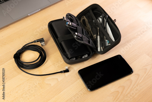 Cable and accessories organiser on a wooden table with a laptop. Black lightning cable, Black bag, charger handbag, smartphone cables, power bank organizer for road trip, work vacation, business trip