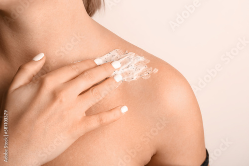 Woman applying scrub on her shoulder against color background, closeup