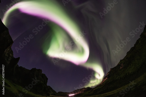 Bright white pink aurora borealis spiral over mountain valley, Iceland © Arctic Mystic