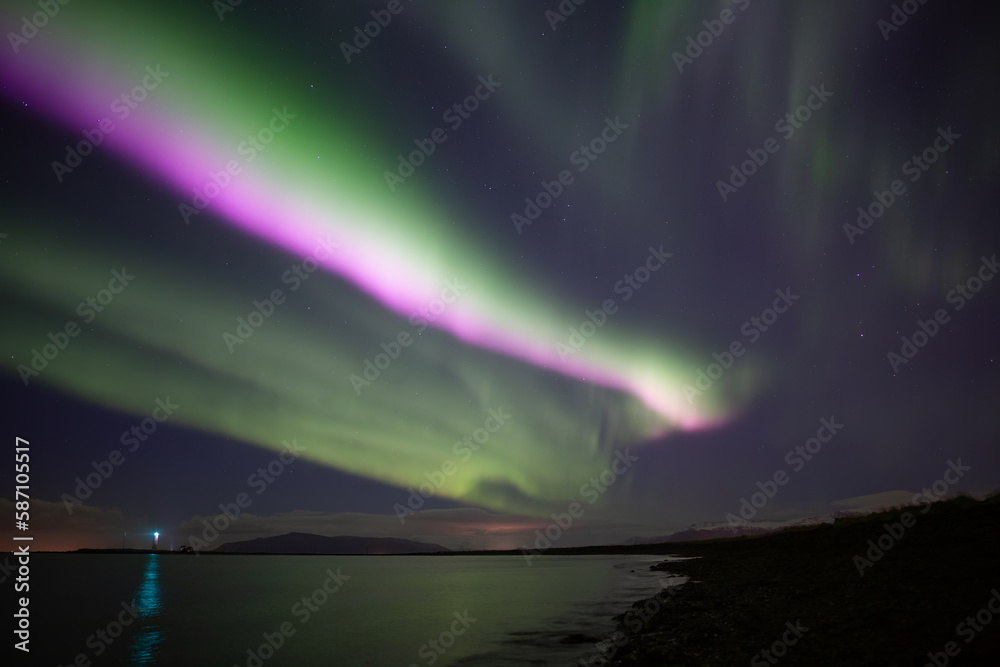 Bright pink aurora borealis over ocen, Grotta lighthouse Iceland