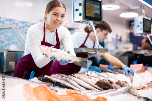 Fotografie Woman seller of fresh fish advises buyer to buy hake fresh fish