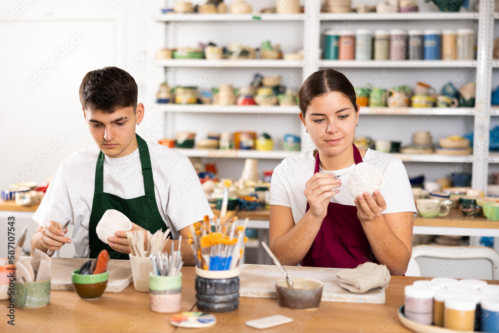 Fototapeta premium Young woman and young man making clay ceramic cups in workshop