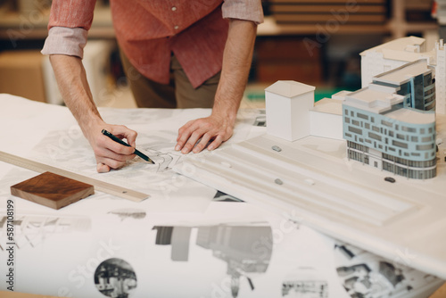 Cropped image of an architect drawing on a blueprint beside building models