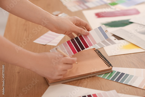 Female artist with paint color palette writing in notebook at table, closeup