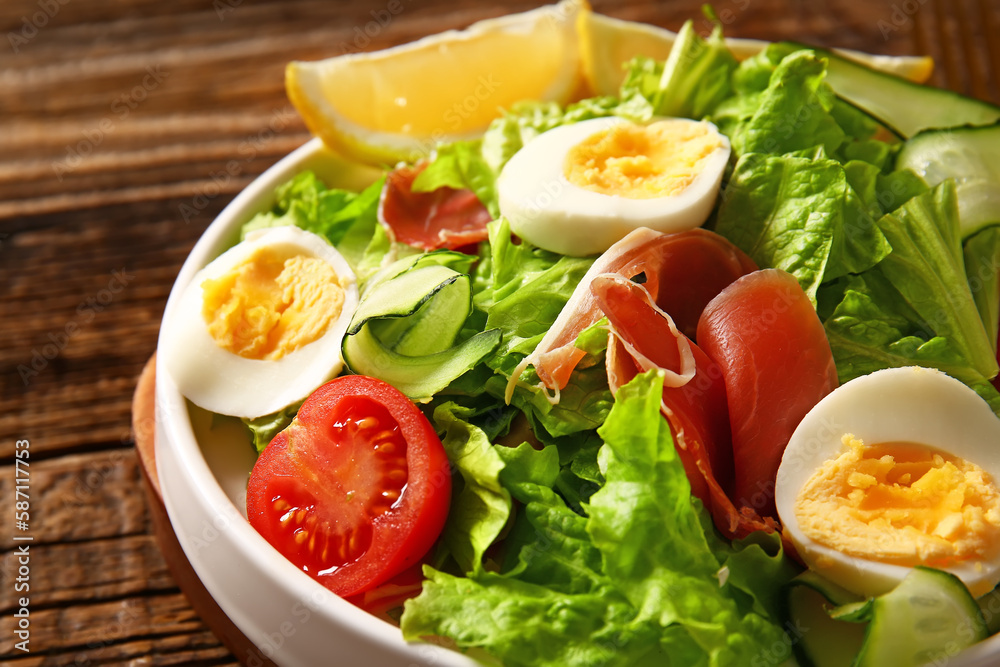 Plate of delicious salad with boiled eggs and jamon on brown wooden background Plate of delicious salad with boiled eggs and jamon on brown wooden background