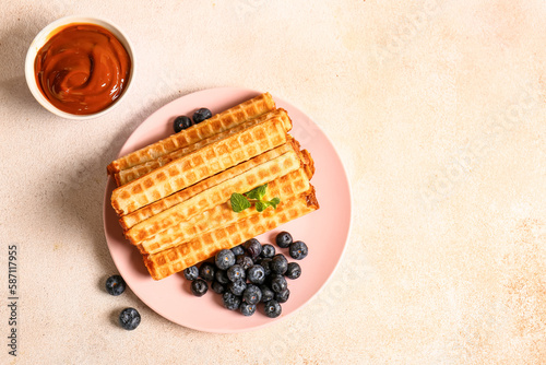 Plate of delicious wafer rolls with boiled condensed milk and blueberries on grey grunge background photo