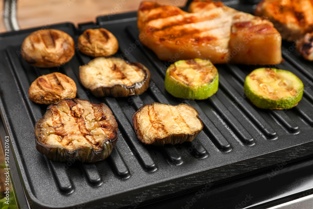 Modern electric grill with tasty vegetables and steaks on table, closeup Modern electric grill with tasty vegetables and steaks on table, closeup