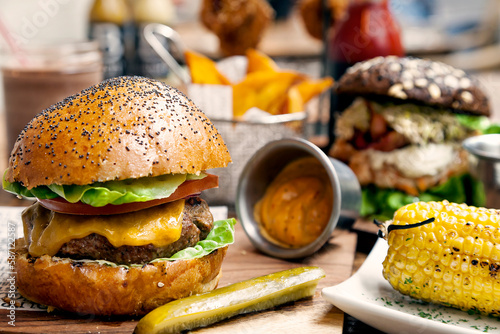 Gourmet cheeseburger with poppy seed freshly baked bun, dill pickles, spicy sauce, and sweet yellow corn cob. 
