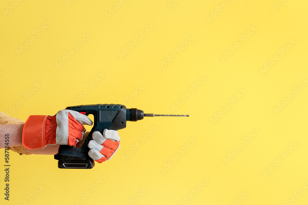 Worker with electric drill on yellow background