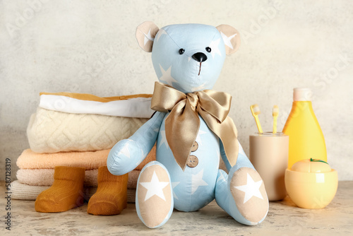 Toy bear with baby clothes and accessories on table near light wall