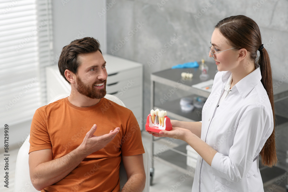 Doctor with educational model of dental implant consulting patient in clinic