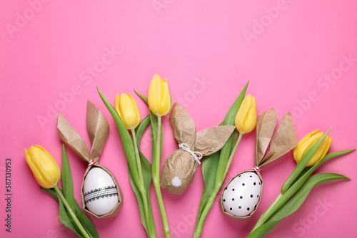 Easter bunnies made of craft paper and eggs among beautiful tulips on pink background, flat lay
