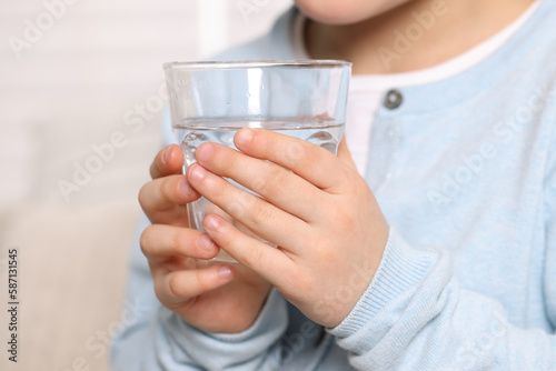 Little girl holding glass of fresh water indoors, closeup
