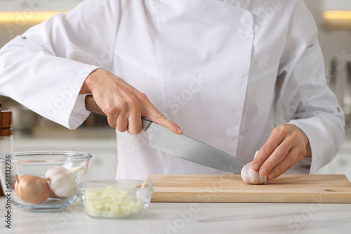 Professional chef cutting garlic at white marble table indoors, closeup