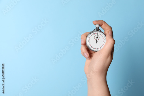 Woman holding vintage timer on light blue background, closeup. Space for text