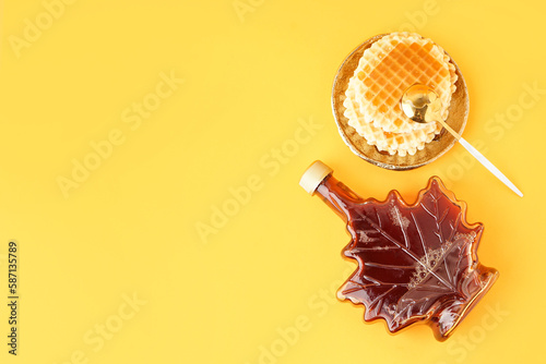 Waffles with bottle and spoon of tasty maple syrup on yellow background