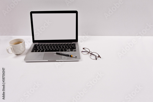 A laptop, a pen, and glasses are placed with a coffee cup