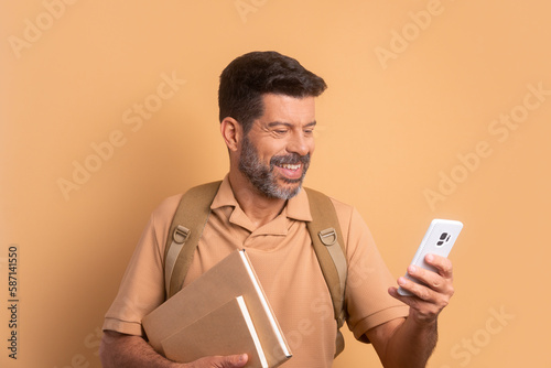 joyful senior man checking smartphone  in beige studio background. learn, school, student life concept. © Vergani Fotografia