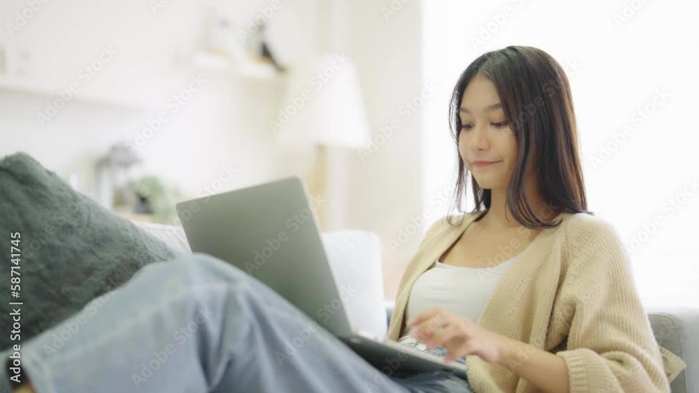 Young asian woman using laptop while seated on couch at home