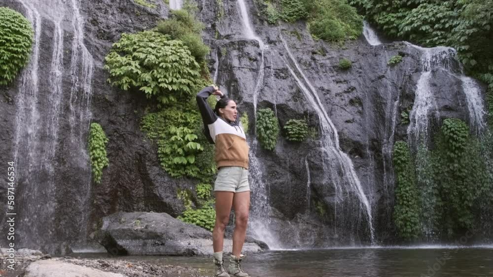 Travel and freedom. woman enjoying tropical waterfall view. Waterfall and woman traveler in Bali, Indonesia. girl who proudly standing with his arms raised in front of water wall of mighty waterfall. Travel and freedom. woman enjoying tropical waterfall view. Waterfall and woman traveler in Bali, Indonesia. girl who proudly standing with his arms raised in front of water wall of mighty waterfall.