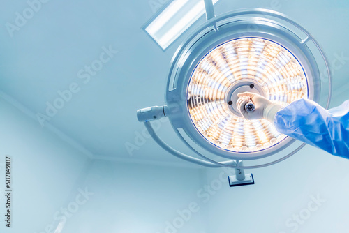 Doctor or surgeon in blue gown holding surgical lamp to adjust light inside operating theatre with space in background.People did surgery in hospital.Nurse with medical glove in operating room. photo