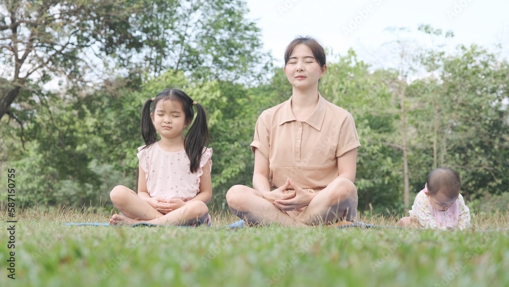 Asian young mother and daughter sitting in yoga asana poses with adorable little baby girl playing naughty on mat yoga in park. Asian young mother and daughter sitting in yoga asana poses with adorable little baby girl playing naughty on mat yoga in park.