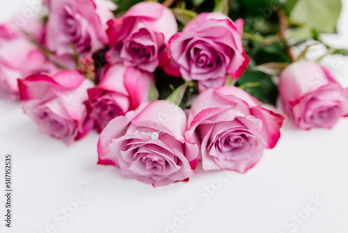 A bouquet of beautiful pink roses with a white gold engagement ring with diamonds on a white background. Fresh flowers on a white canvas. Wedding bouquet and wedding rings. Surprise marriage proposal.