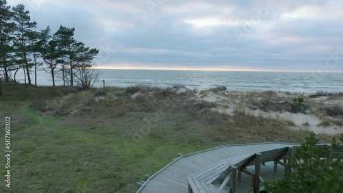 Establishing aerial view of wooden boardwalk at Baltic sea coastline, Sunset hiking trail with benches, Nordic woodland pine forest, overcast evening before the sunset, drone shot moving forward low photo