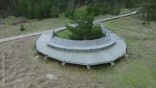 Establishing aerial view of wooden boardwalk at Baltic sea coastline, Sunset hiking trail with benches, Nordic woodland pine forest, overcast evening before the sunset, drone shot moving back tilt up photo