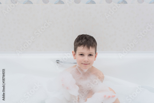 Happy boy takes a bath with lush foam playing with bubbles. Personal hygiene, healthcare concept