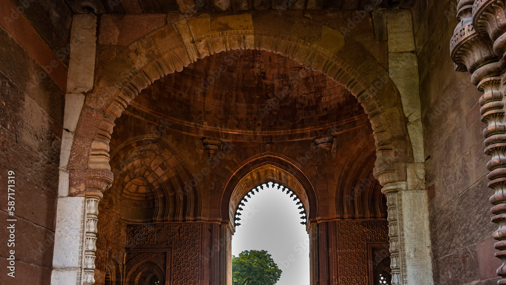 Details of the architecture of the ancient temple complex Qutub Minar. The arches of the sandstone building are decorated with carvings. The blue sky is visible in the opening. India. Delhi