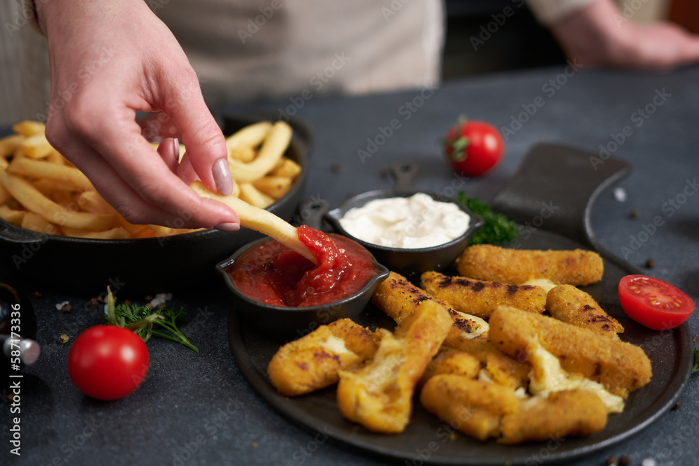 Woman dips french fries into dip sauce with Cheese fried mozzarella sticks on a table