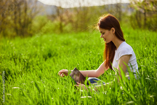 woman working on a laptop while sitting in the tall grass on the street photo